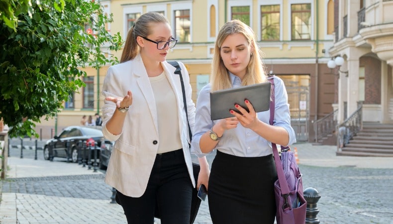 Zwei Frauen im Gespräch draussen, eine mit iPad, diskutieren Corporate Communication Zusammenarbeit mit dem Fachbereich