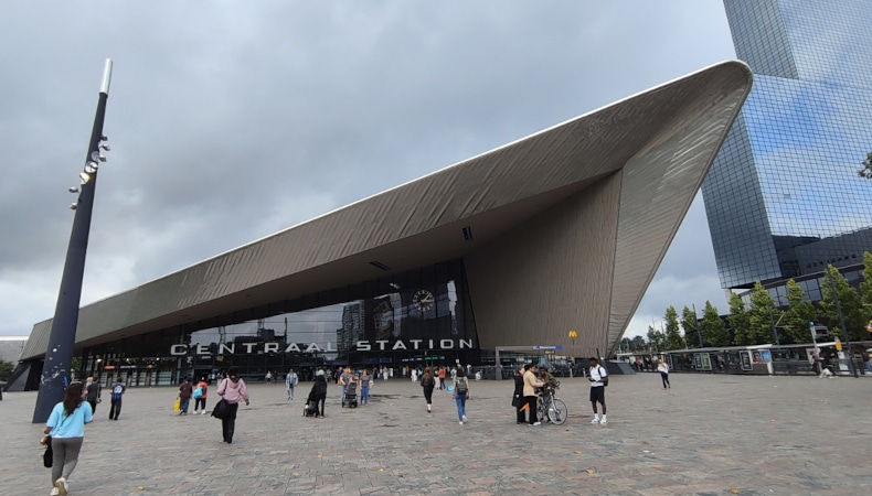 otterdam Centraal mit markantem, spitz zulaufendem Dach und Stationsplein/Bahnhofsplatz mit Passanten.
